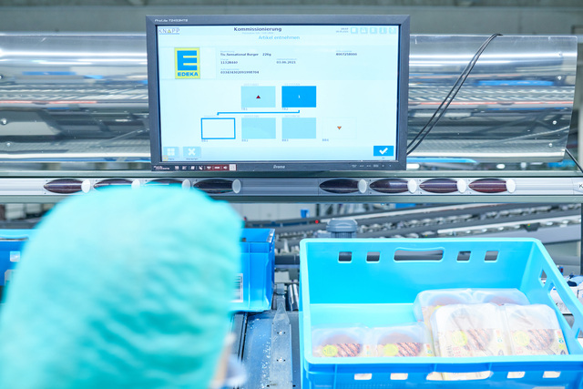 Ein Arbeiter mit Haarnetz betrachtet die Bestandsdaten über blauen Behältern mit verpackten Lebensmitteln - Maximale Frische durch maßgeschneiderte Automatisierung im Werk.