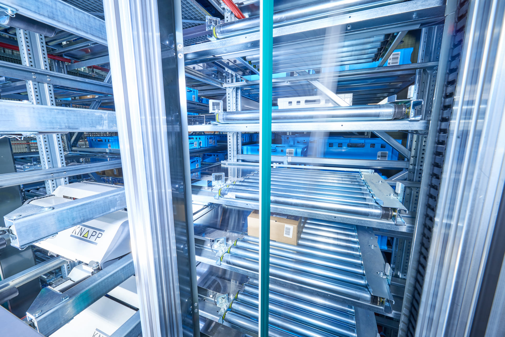 Vue rapprochée d'un système d'automatisation d'entrepôt avec des rouleaux de convoyeurs, des rayonnages métalliques et un carton transporté à travers la structure.