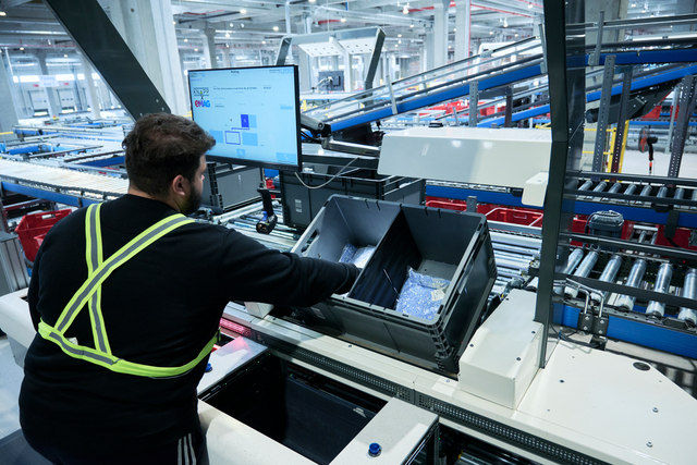 Ein Mann kommissioniert einen Textilartikel bei eMAG an den ergonomischen Pick-it-Easy Arbeitsplätzen mit visueller Hilfe auf einem Bildschirm.