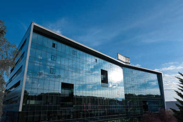 KNAPP-KAG Site 011_Logo bearbeitet_erweitert Modernes Glasgebäude mit spiegelnden Fenstern unter blauem Himmel; die Buchstaben "WAPP News" sind auf einem Schild an der Spitze des Gebäudes zu sehen.