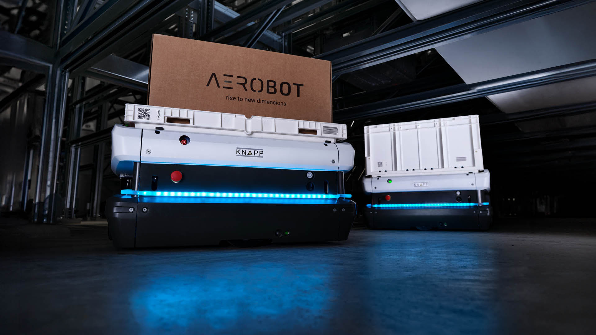 Zwei autonome Lagerroboter, einer davon mit der Bezeichnung "AEROBOT", arbeiten in einer modernen Umgebung, wie sie auf der KNAPP auf der LogiMAT zu sehen ist, mit blau leuchtenden LEDs.
