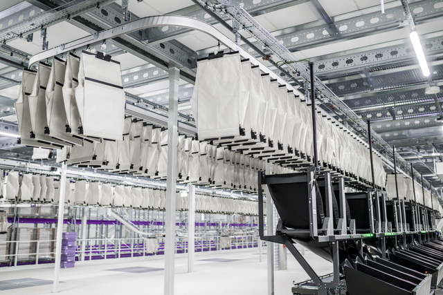 Rows of white fabric bags hang from ceiling tracks in a modern pharmaceutical distribution warehouse with metal beams and bright lighting visible.