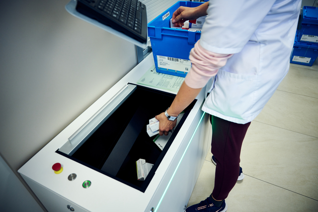 Eine Person in einem Laborkittel sortiert Medikamentenschachteln in eine Maschine ein, was die Art und Weise widerspiegelt, wie Victorinox auf zentrale Verteilung in Kliniken oder Apotheken setzt.