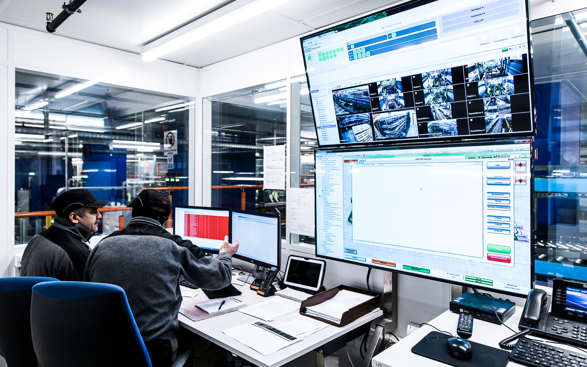 Deux personnes sont assises à des bureaux dans une salle de contrôle lumineuse, où Migros Zurich automatise la livraison de 150 magasins et analyse des données sur de grands écrans.