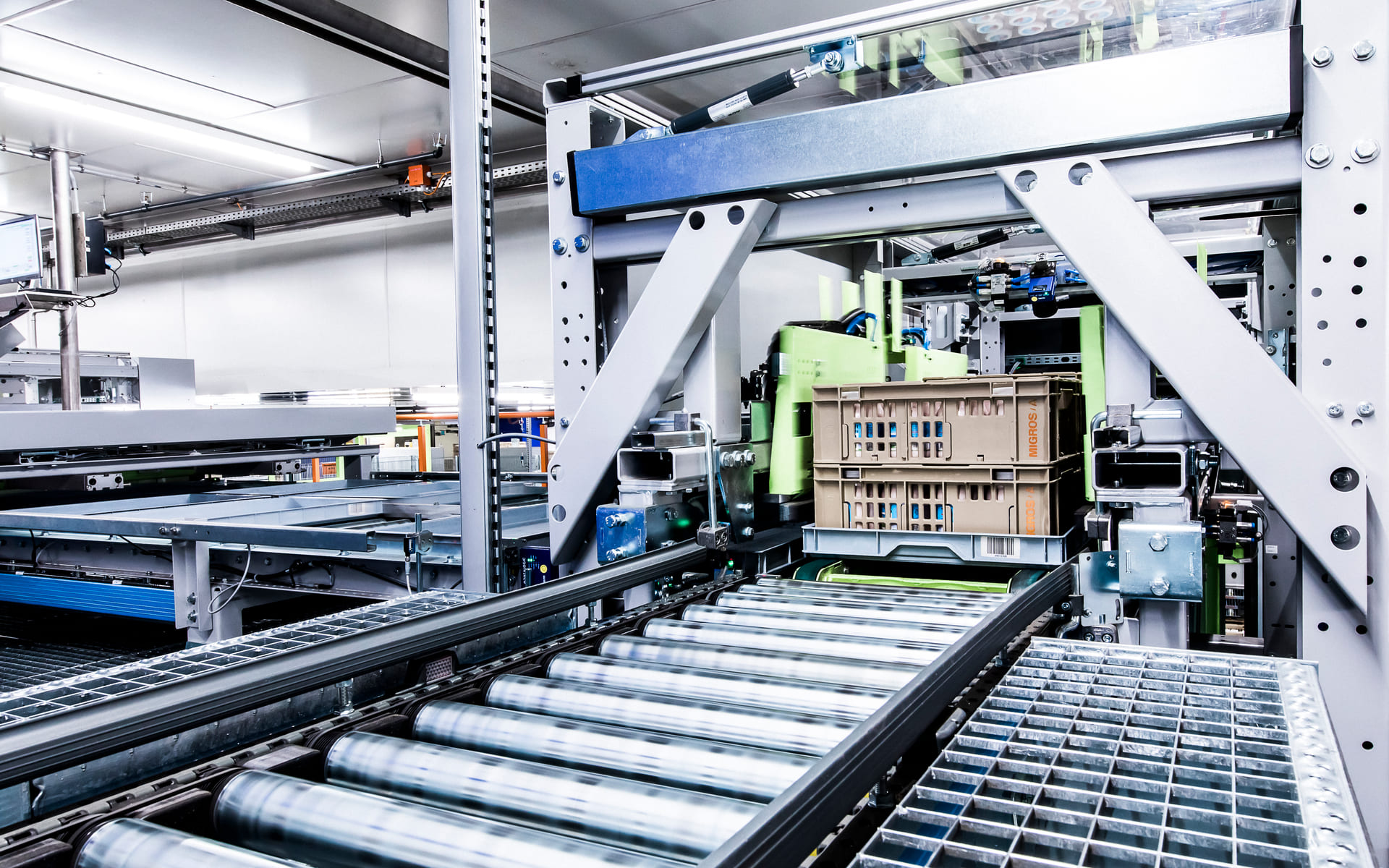 Système de convoyage automatisé dans une usine moderne, avec des caisses transportées et triées par des machines ; des équipements industriels et des rouleaux métalliques sont visibles dans un environnement propre et bien éclairé.