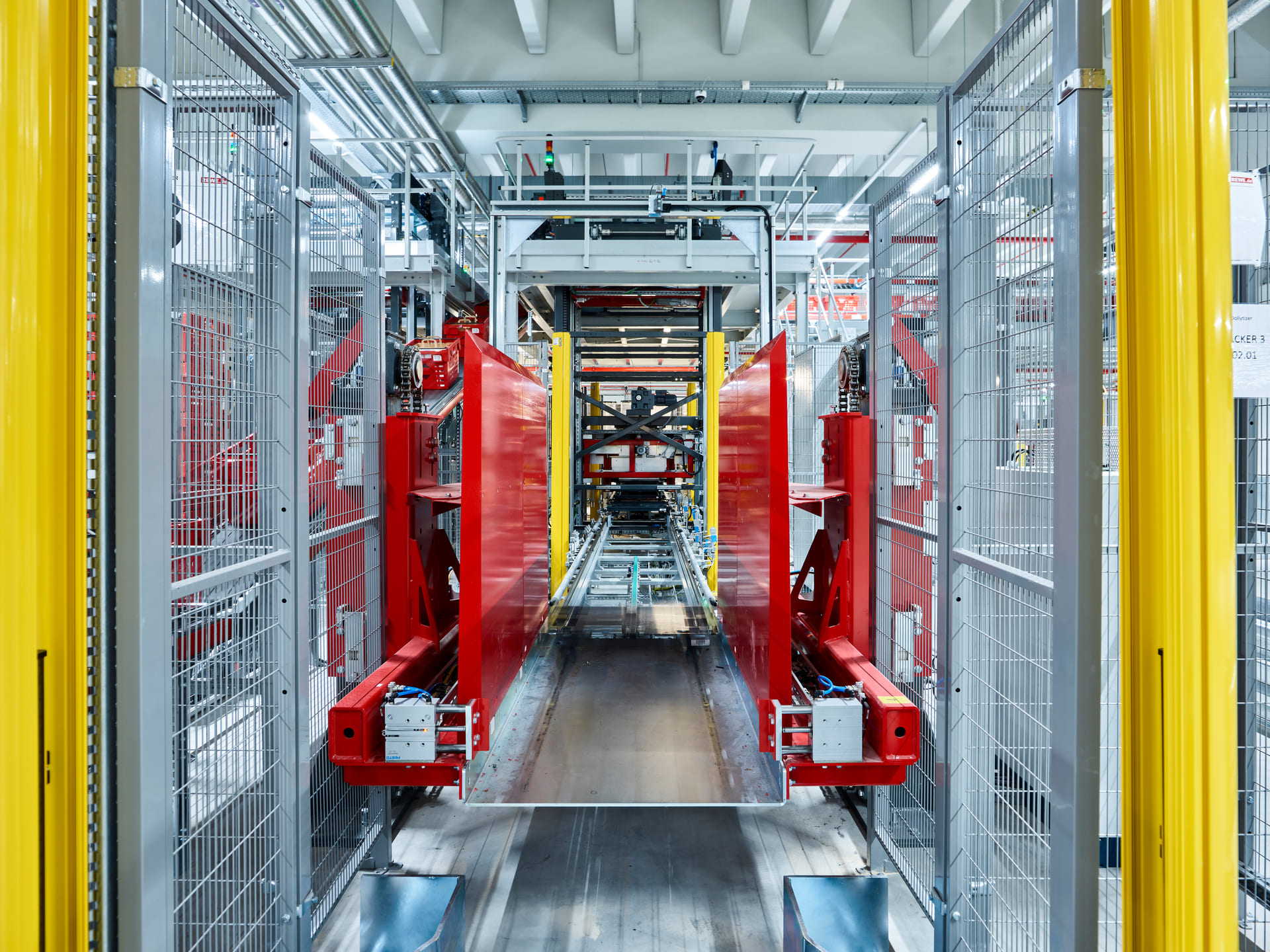 Une chaîne de production automatisée moderne dans une usine, avec une clôture métallique, des poutres structurelles jaune vif et de grands composants de machines rouges le long d'un convoyeur central.