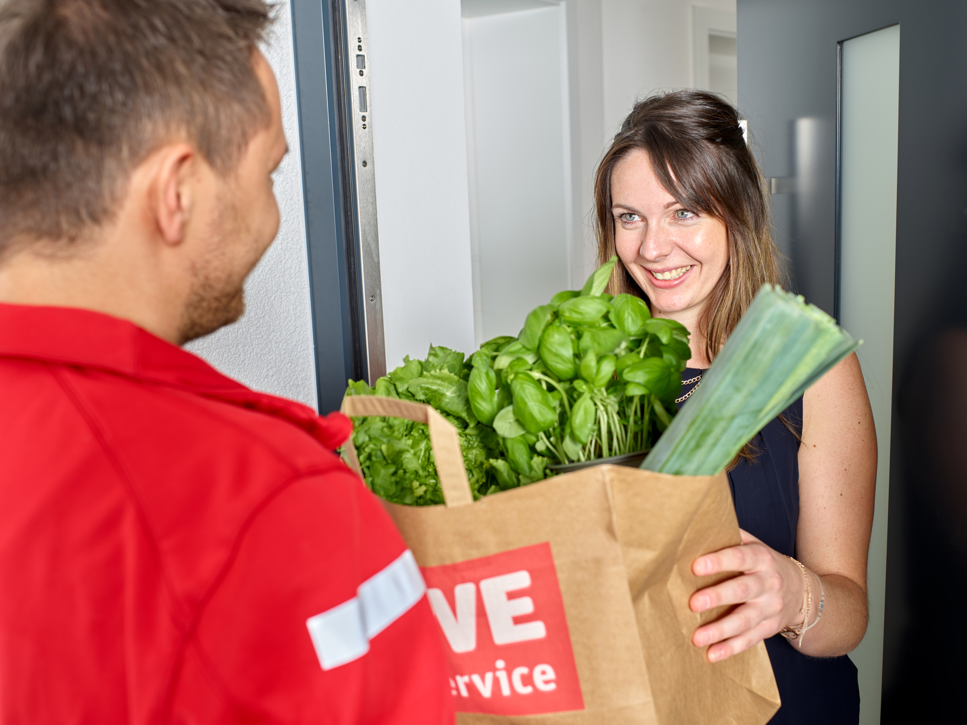 Eine lächelnde Frau erhält eine Papiertüte an ihrer Tür, während Technologien den Online-Lebensmittelhandel revolutionieren.