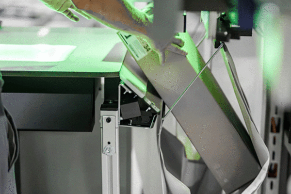 Eine Person übergibt eine Schachtel an eine Sortertasche an einem Pick-it-Easy-Pocket-Arbeitsplatz.