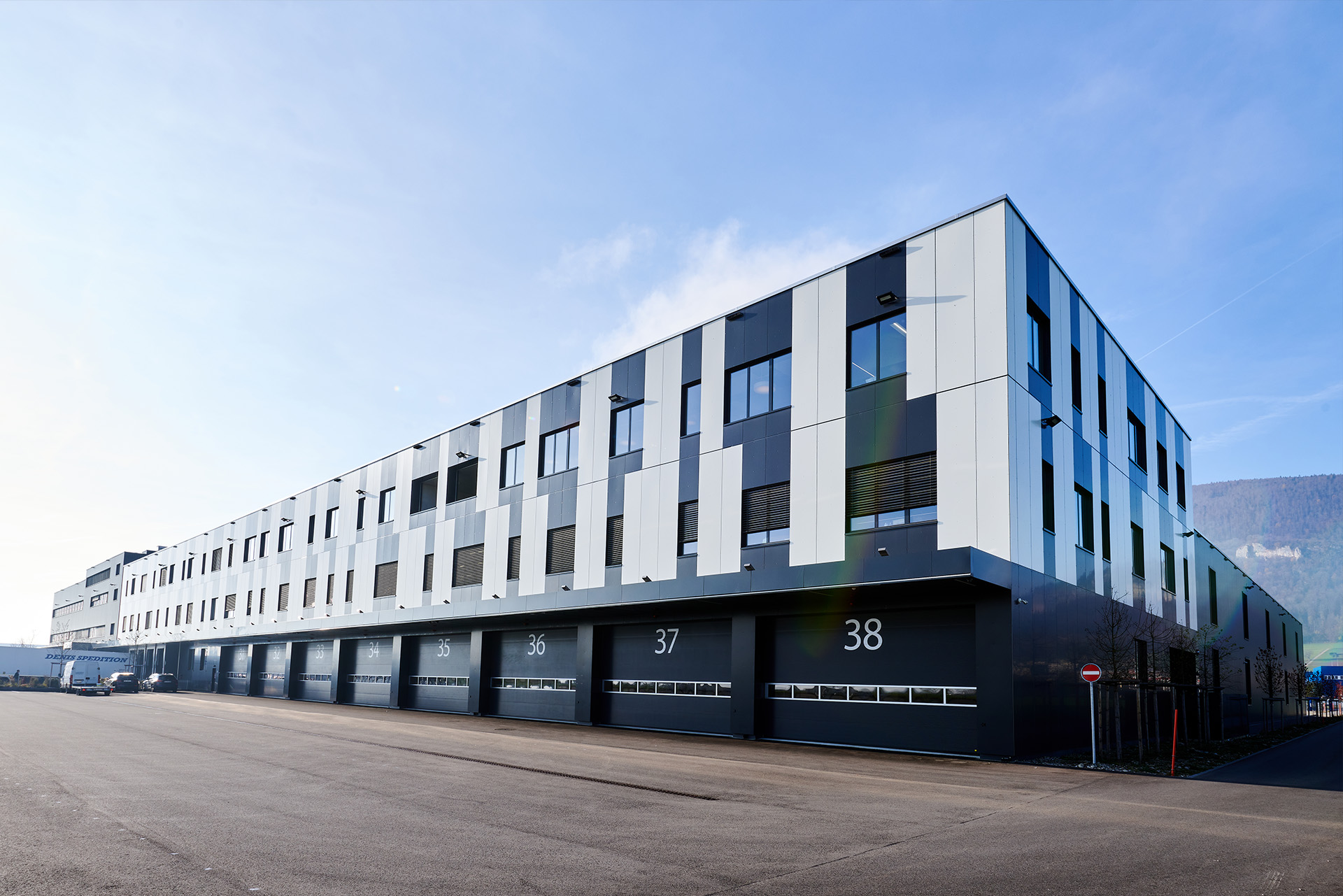 Moderno edificio industrial con puertas de garaje numeradas, grandes ventanales y un cielo azul despejado al fondo.