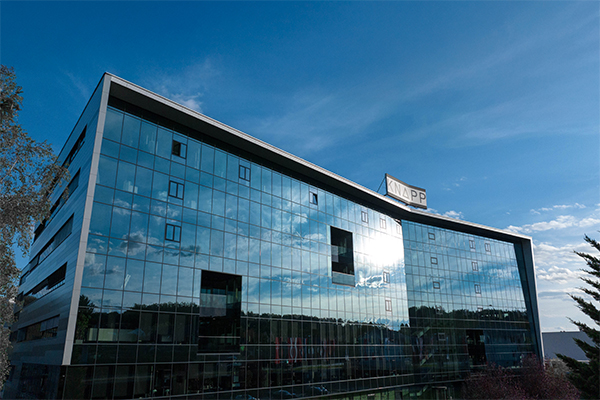 knapp_ag_standort Immeuble de bureaux moderne en verre avec un ciel bleu et des nuages se reflétant dans ses fenêtres ; un panneau sur le toit indique "APP.