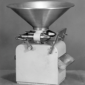 A black and white photograph of an old machine that can fill donuts with jam.