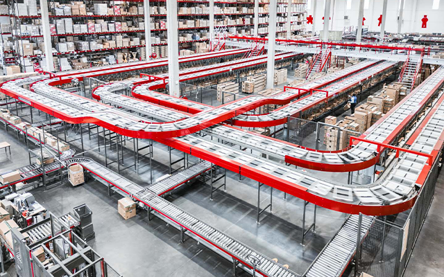 Un gran almacén con extensas cintas transportadoras que serpentean por estanterías llenas de cajas y paquetes, mostrando un centro organizado de logística y distribución.