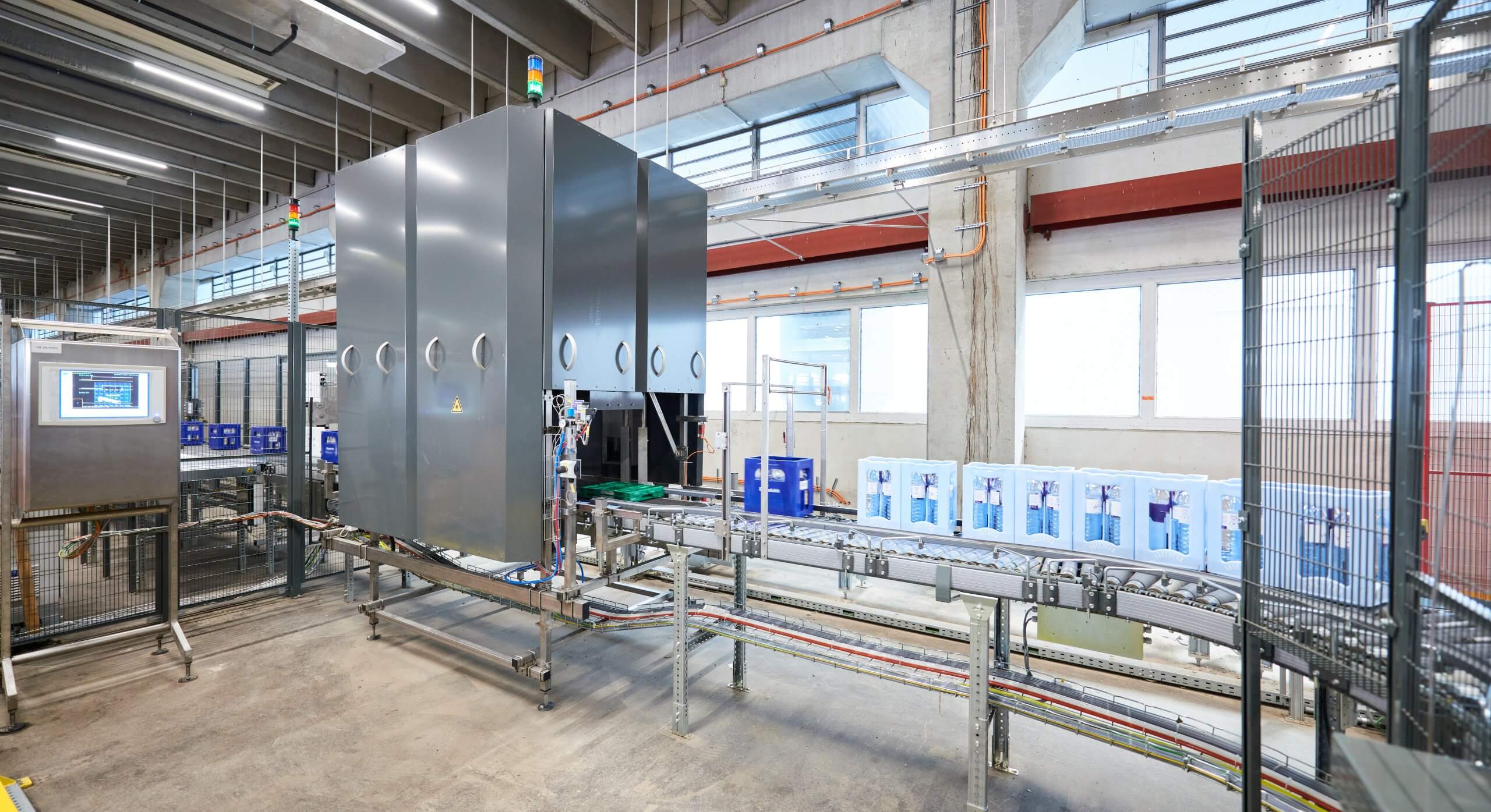 The image shows a logo recognition machine with a monitor. Various beverage crates are being conveyed into the machine on a conveyor.