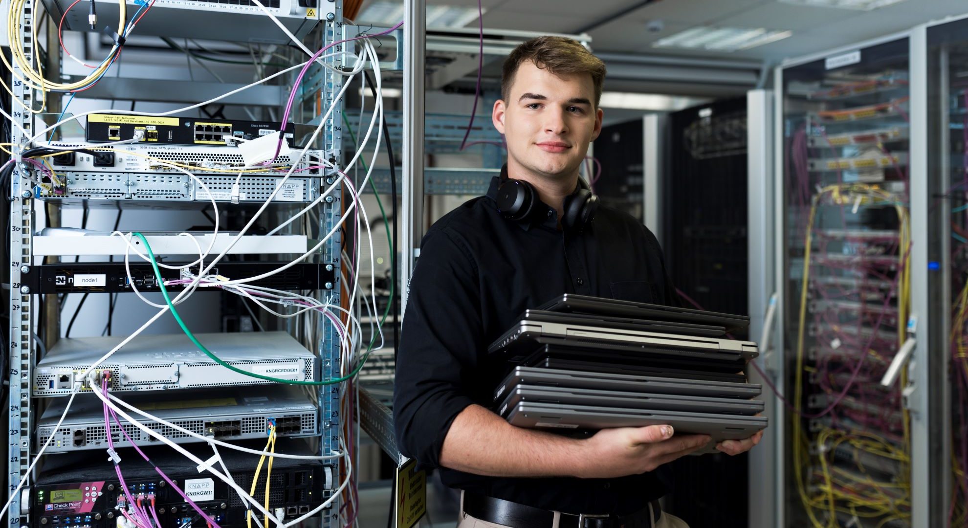 _O8A6462-Web-4000px Ein Lehrling arbeitet stehend an einem Laptop und lächelt dabei in die Kamera.