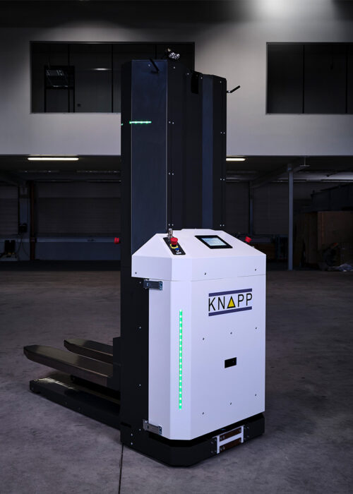 Open Shuttle Fork – AMR for pallet transport Una carretilla elevadora automatizada con el logotipo de KNAPP se encuentra en un almacén con poca luz, lista para su uso.