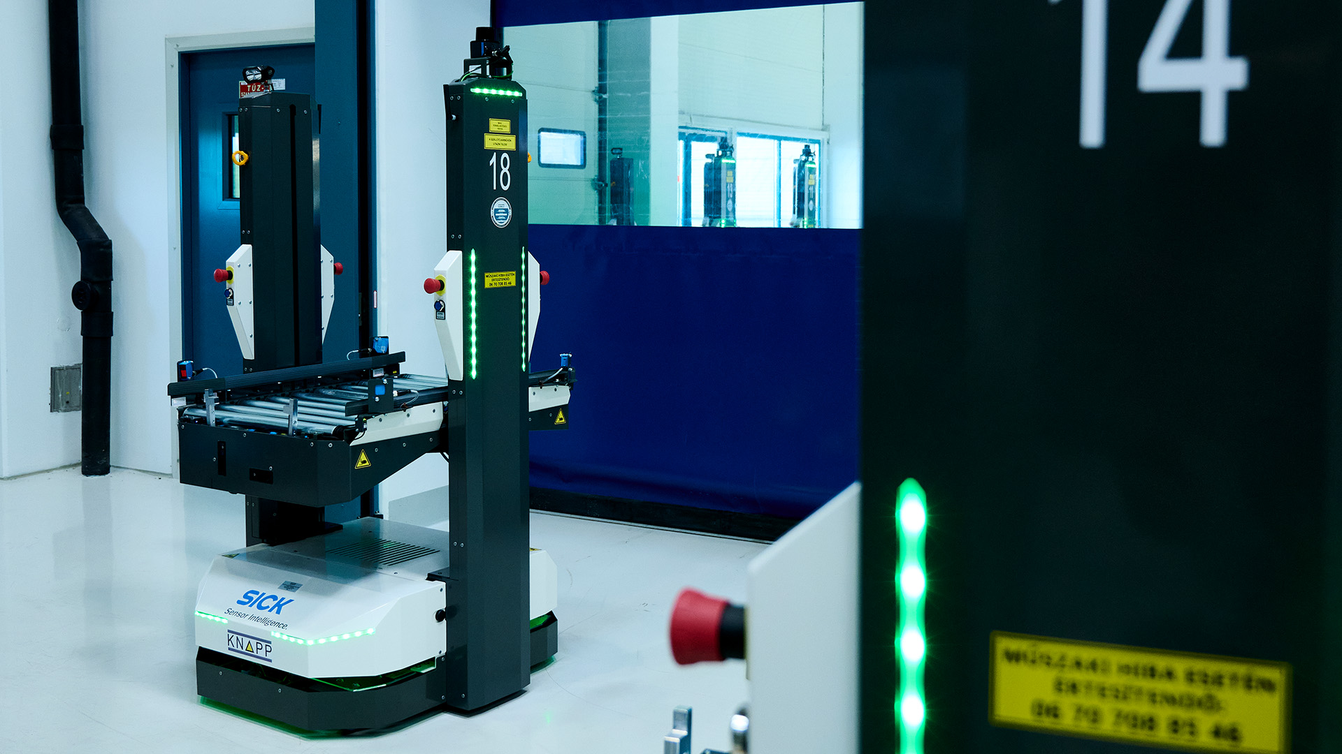 Ein autonomer Roboter mit Fördersystem und grünen Leuchten demonstriert die Integration von AMRs in einer sauberen, modernen Anlage mit blauen und weißen Wänden und reflektierenden Böden.