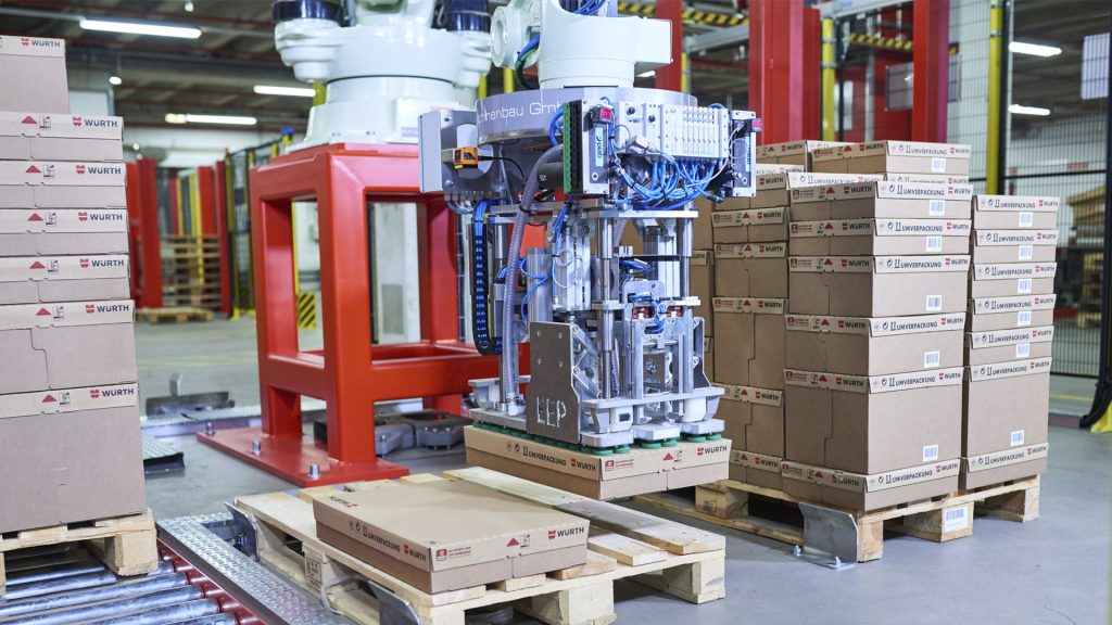 Paletizado para la industria del plástico Un robot industrial agarra una caja de cartón y la apila sobre un palet.