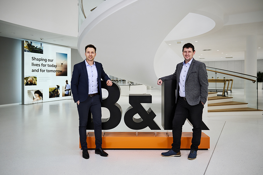 Sustainable partnership between B&R and KNAPP Michael Humer and Christian Brauneis-Lieb in business attire standing in front of the B&R logo in a large, modern hall.