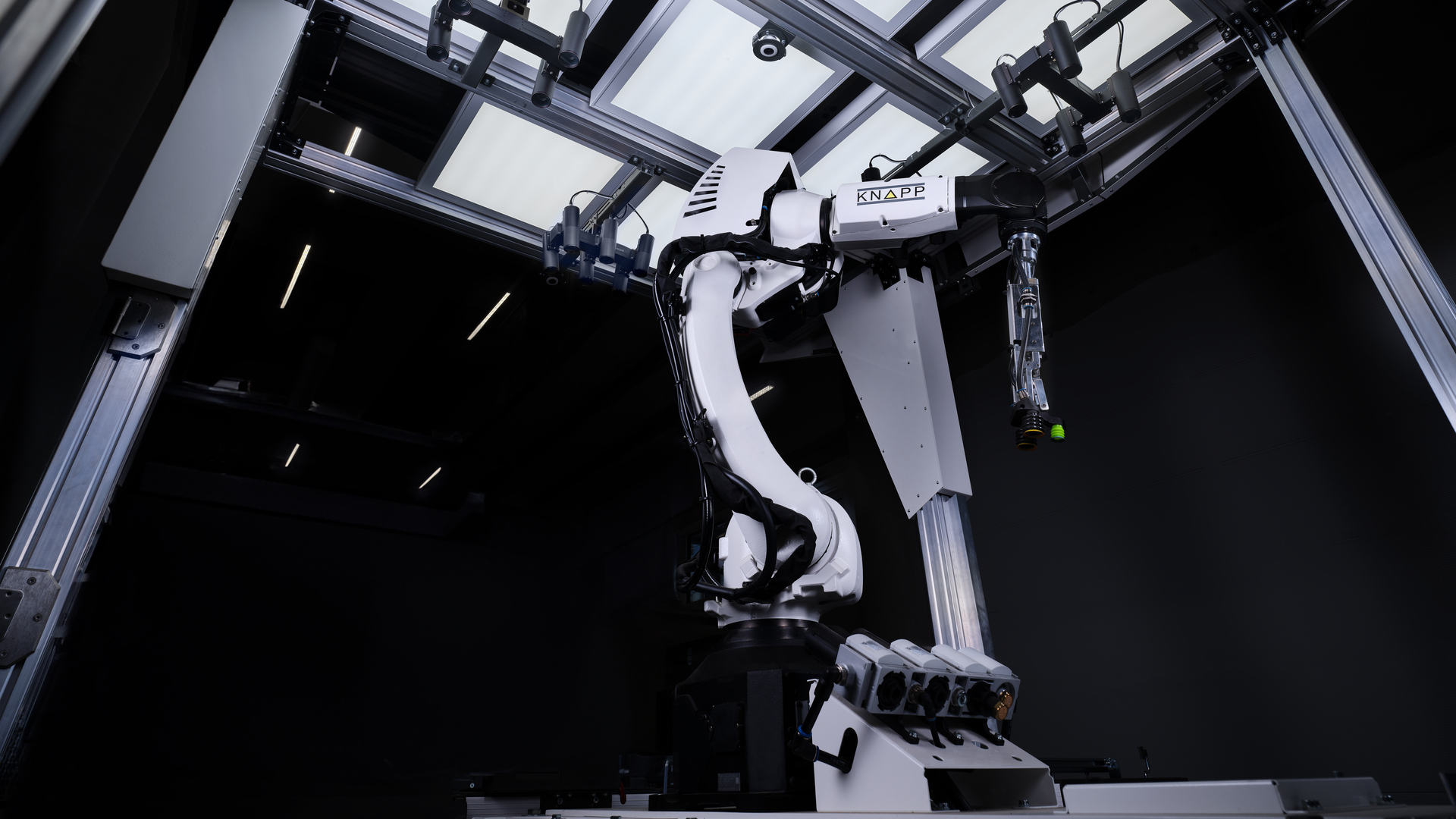 Ein weißer Pick-Roboter arbeitet in einem modernen Gehäuse mit Metallrahmen, Oberlicht und dunklem Hintergrund.