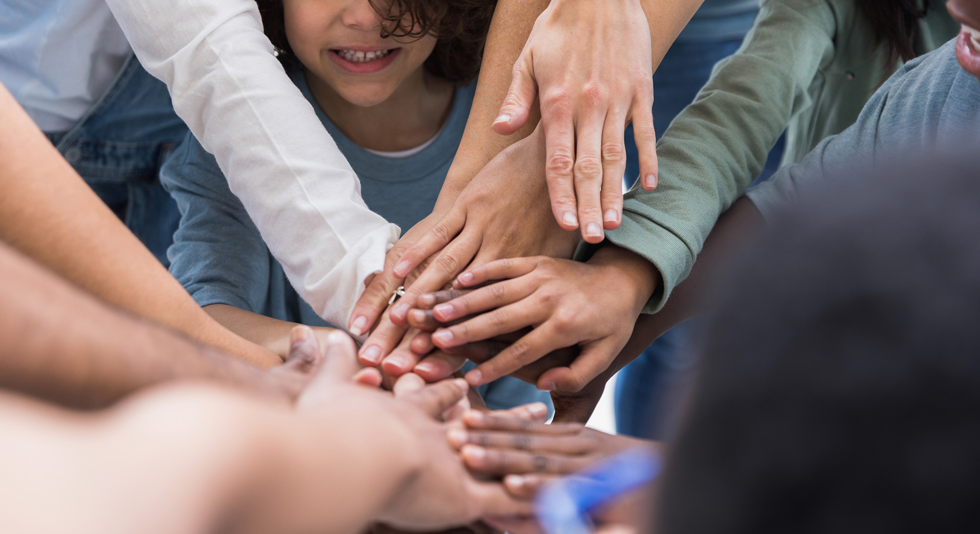 A multi-racial group of people place their hands together to symbolize their unity.