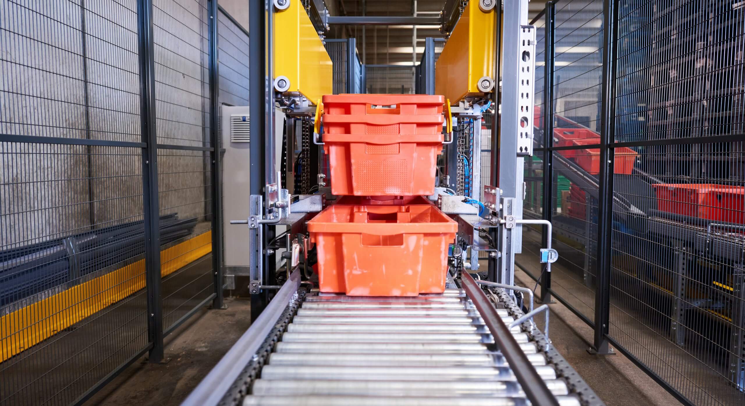 Front view of a fully automatic destacking machine that separates totes for meat and meat products. The tote stacks are transported to the machine on the conveyor system. Clamps grip the totes and separate them. The totes are placed on the conveyor system one by one and move on for further processing.