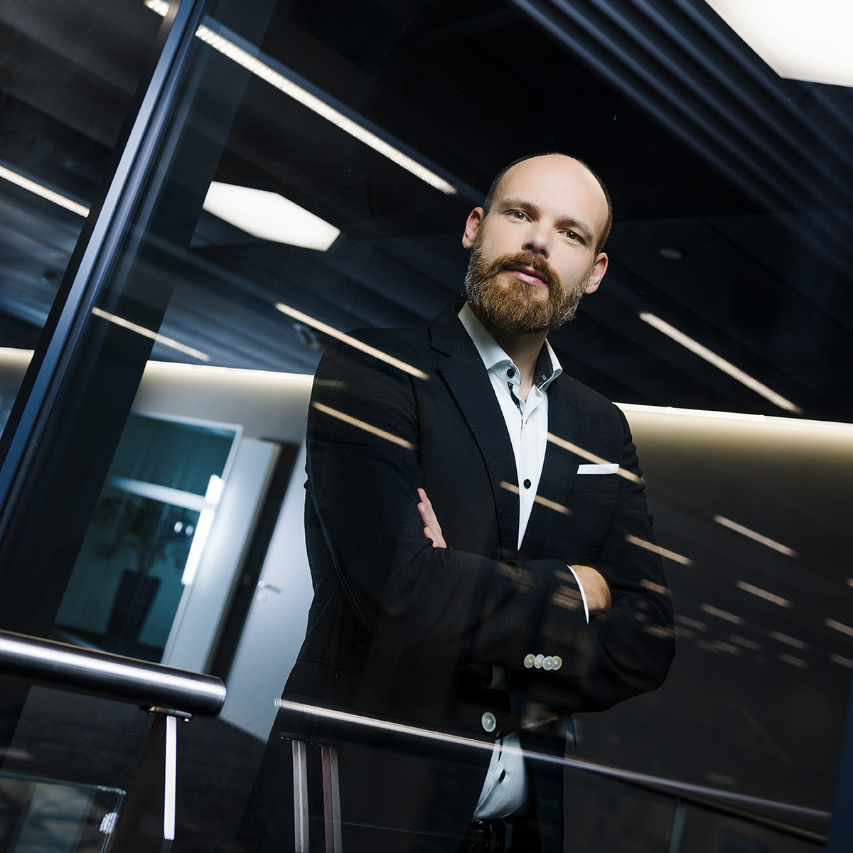 Thomas_Ulz Thomas Ulz steht mit Armen verschränkt vor einer Scheibe, die Licht reflektiert.