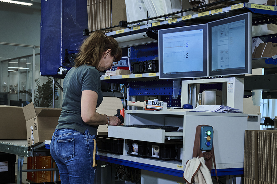 Shipping area of the B&R smart factory A woman is standing at a shipping work station in front of a monitor and packaging material.