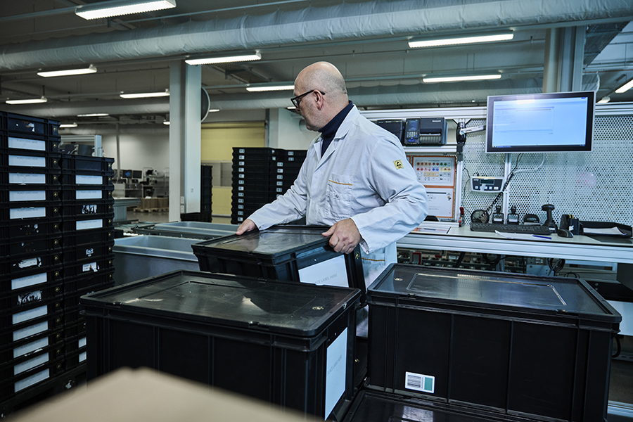 Production supply case study: goods-in at B& A bald man wearing glasses lifts a container towards his work station. There is a screen in the background.