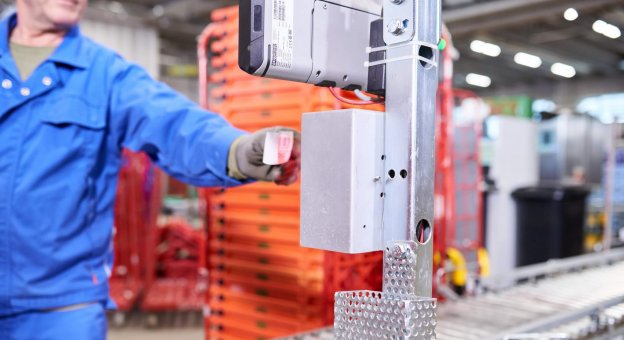 Close-up picture of a Cleanaway employee scanning a ticket at a terminal for booking according to store. This is how empties receiving starts. There are unsorted empties in the background that will soon be placed on the conveyor system.